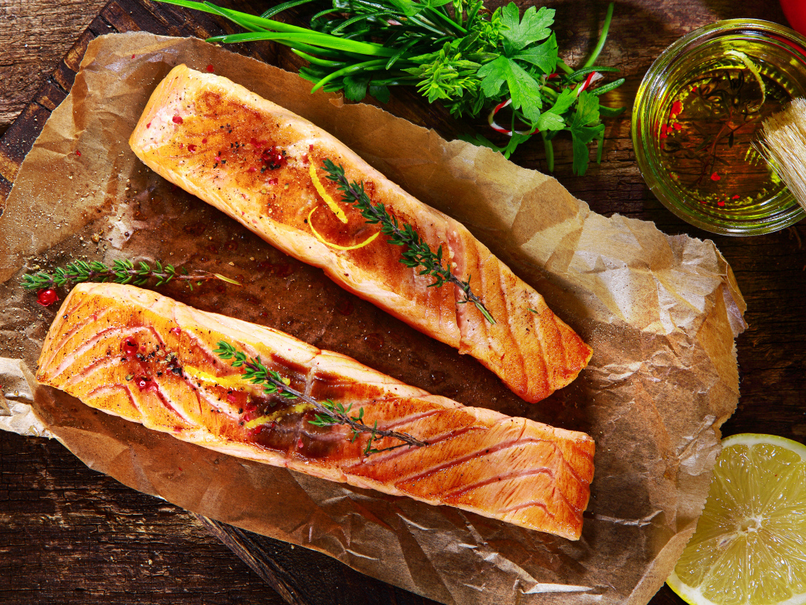 Два куска запеченной рыбы на столе с оливковым маслом и зеленью