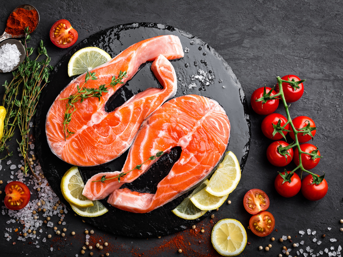 Два куска красной рыбы с овощами на черном фоне