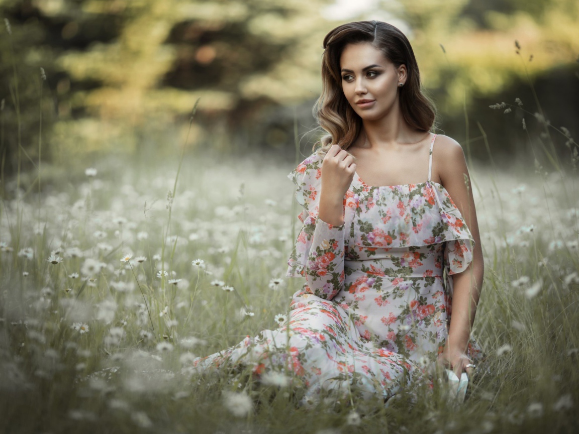 Красивая девушка в сарафане сидит на поляне с ромашками 