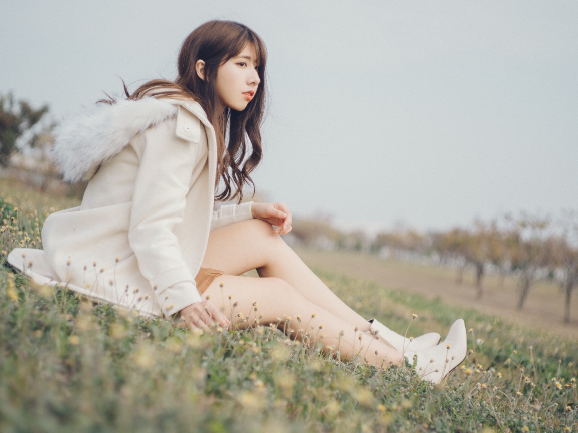 Девушка азиатка в пальто сидит на траве