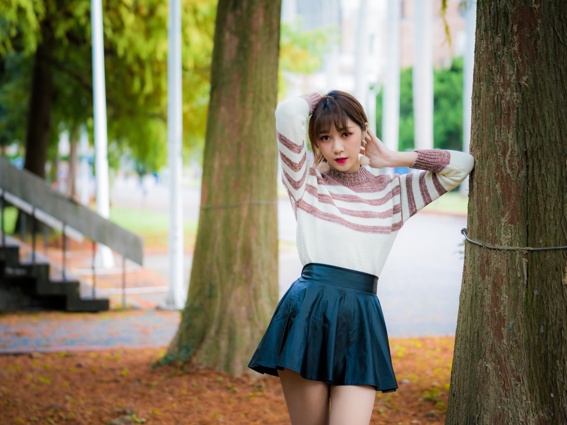 Девушка азиатка стоит в короткой юбке у дерева