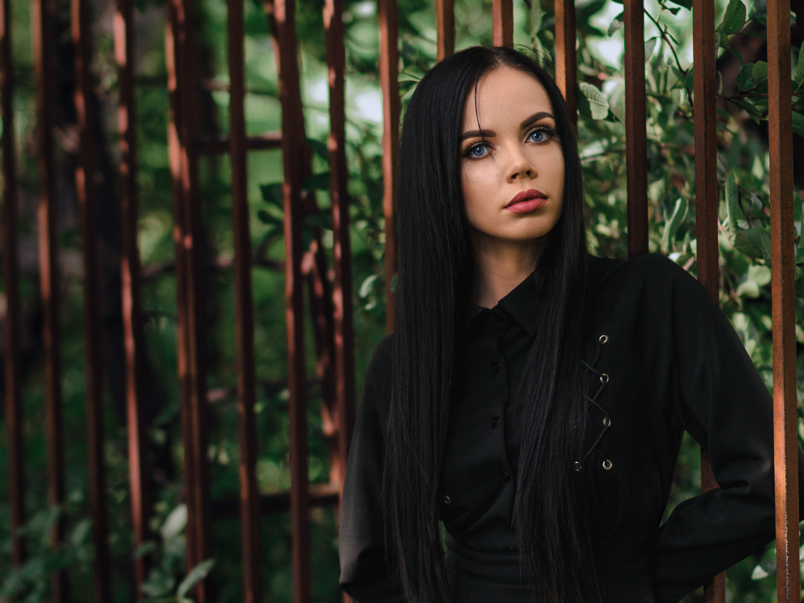 Красивая голубоглазая девушка в черном платье у железного забора