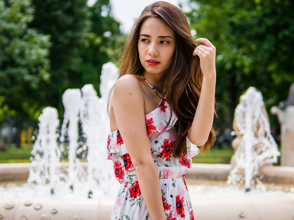 Красивая шатенка в цветастом платье у фонтана летом