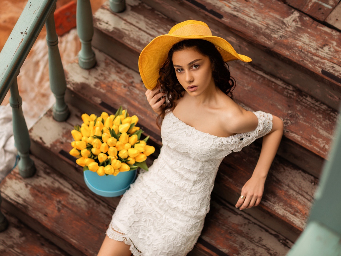 Красивая девушка в белом платье и желтой шляпе на ступеньках с букетом тюльпанов