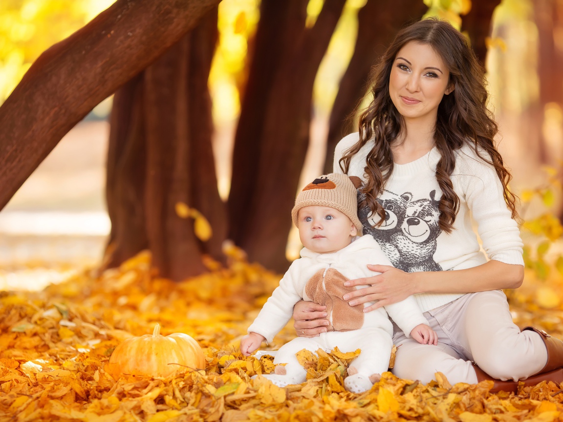Красивая девушка сидит с грудным ребенком на опавшей листве