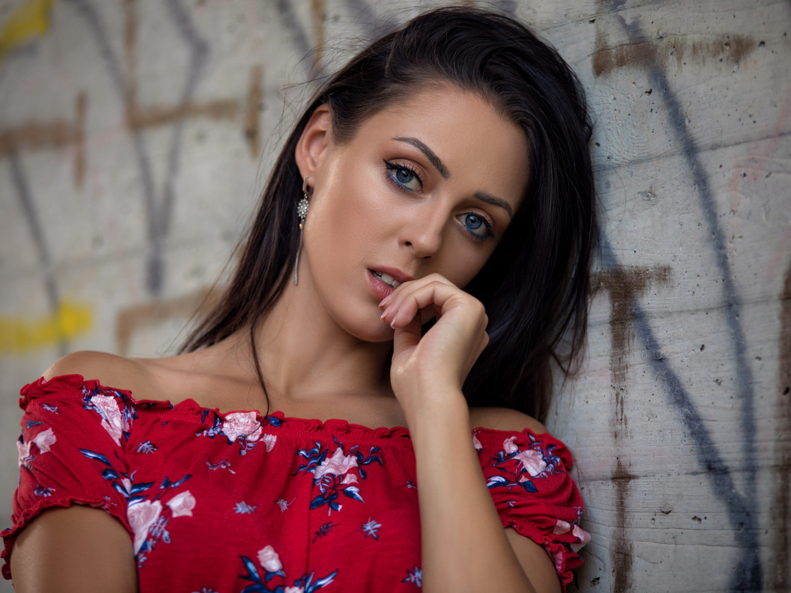 Голубоглазая брюнетка стоит в платье стоит стены