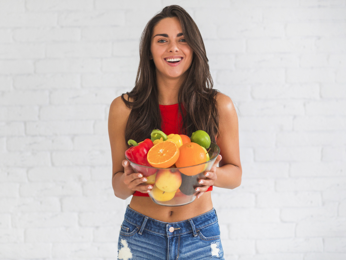 Брюнетка с миской фруктов на фоне стены