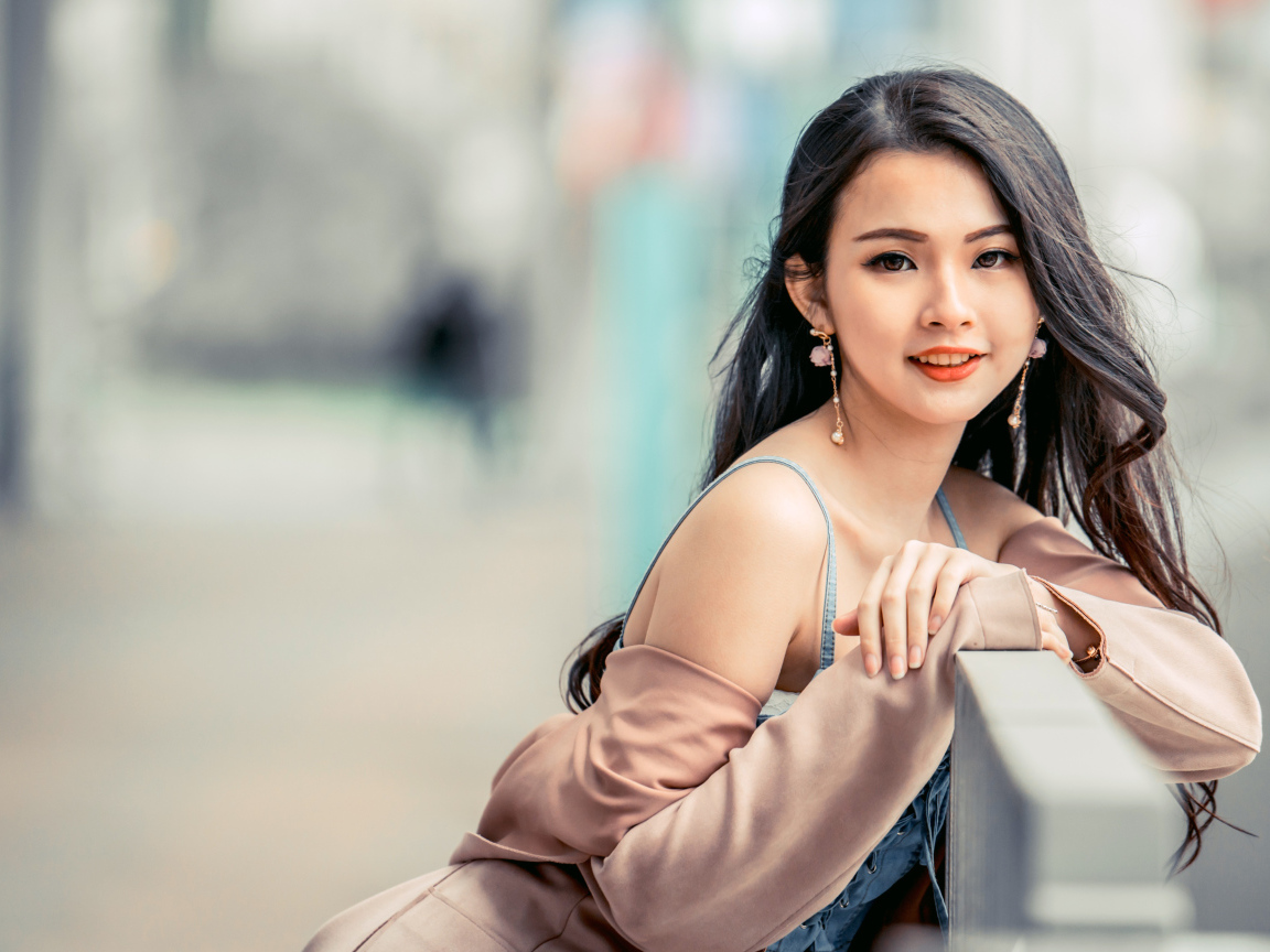 Очаровательная девушка азиатка сидит на лавке