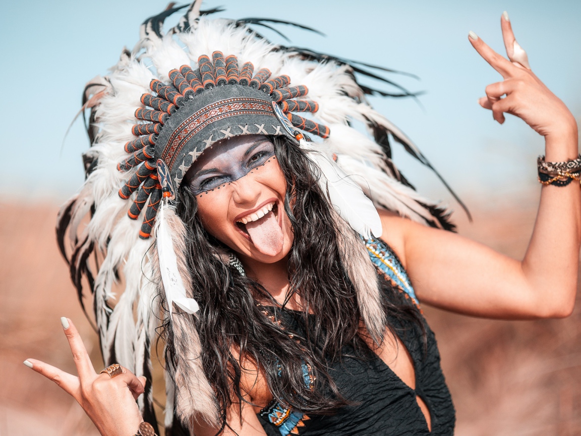 Веселая девушка с высунутым языком в костюме индейца