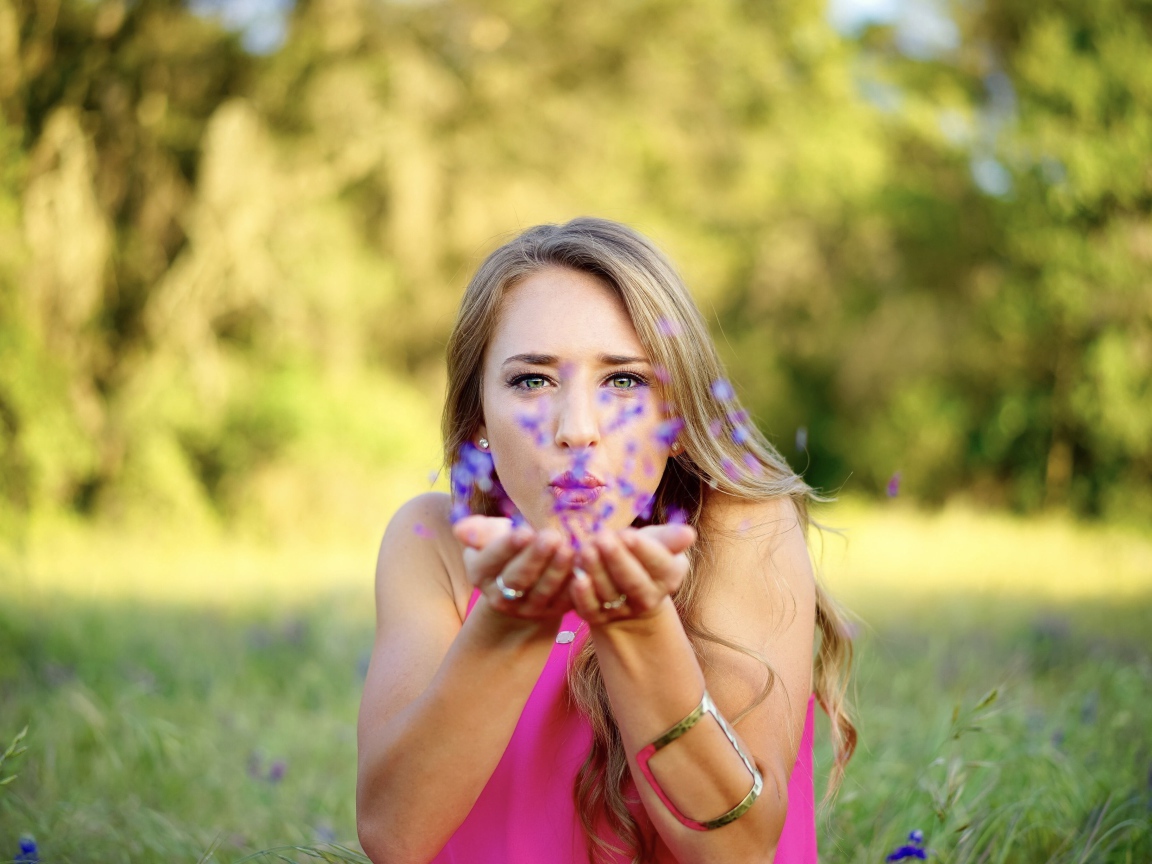 Девушка сдувает лепестки с ладоней 