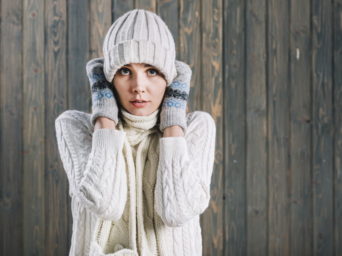 Девушка в варежках поправляет шапку на голове
