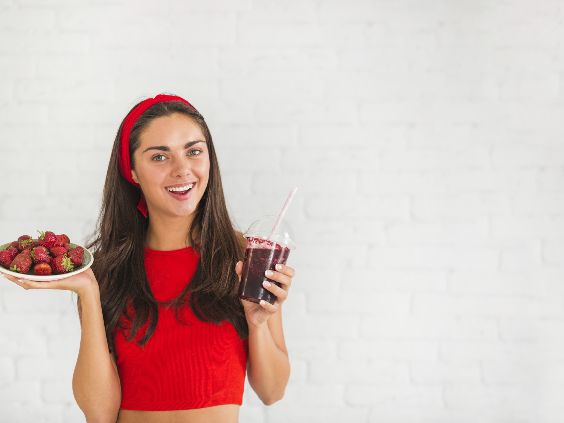 Улыбающаяся девушка с клубникой и смузи в руках