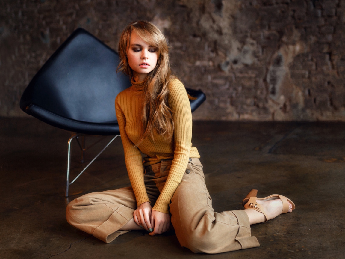 Девушка сидит на полу около черного кресла 