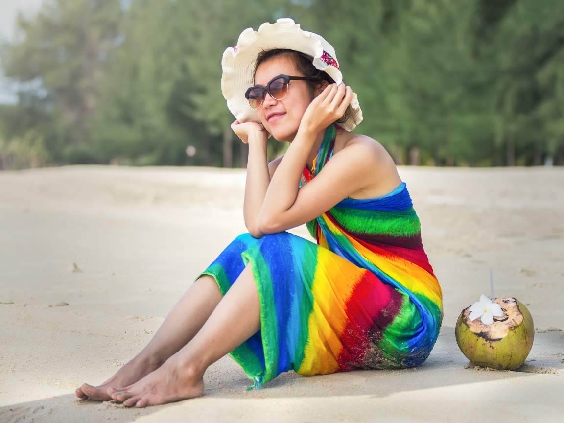 Молодая азиатка сидит на берегу с кокосом