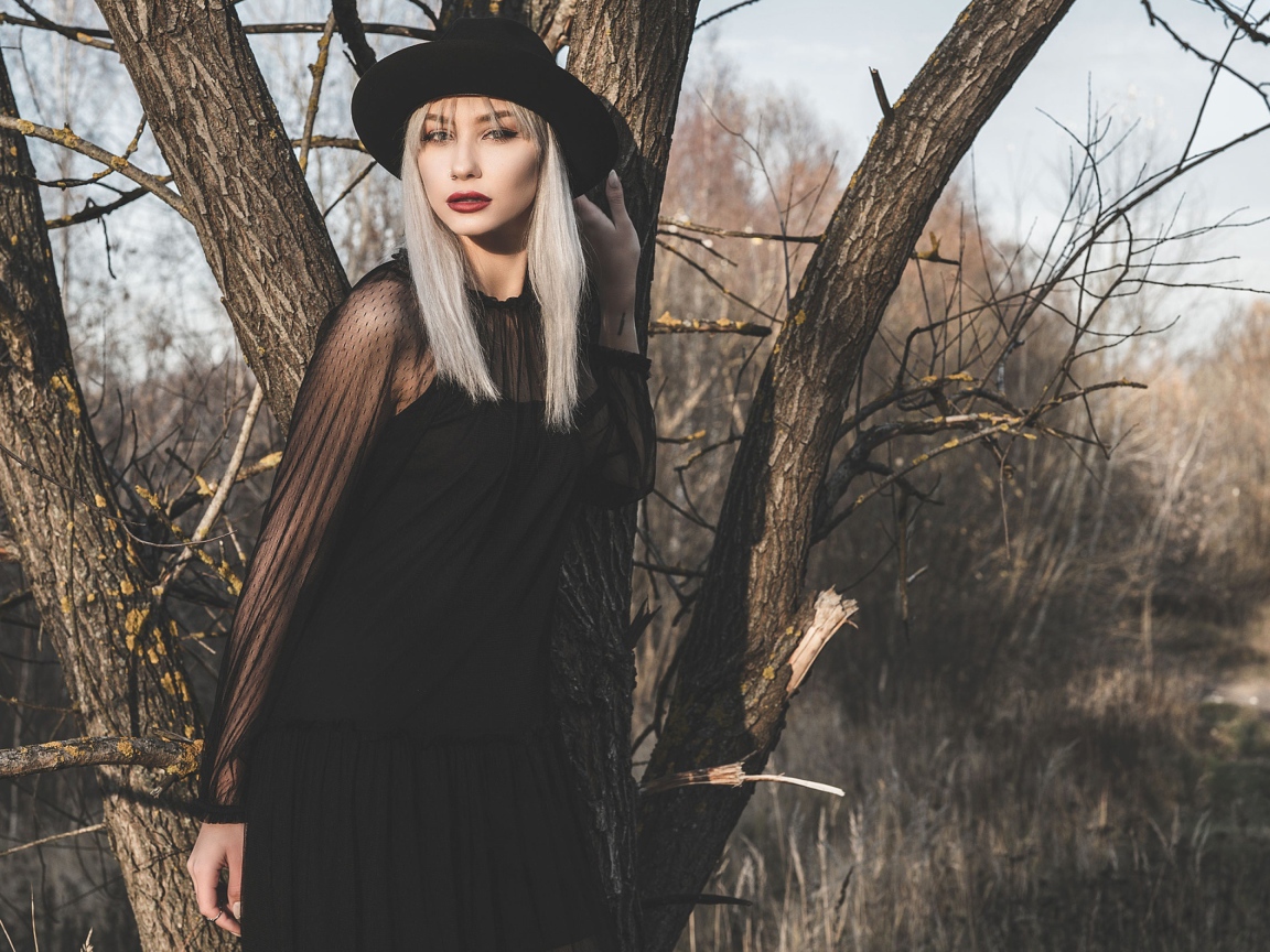 Молодая блондинка в черной шляпе у дерева