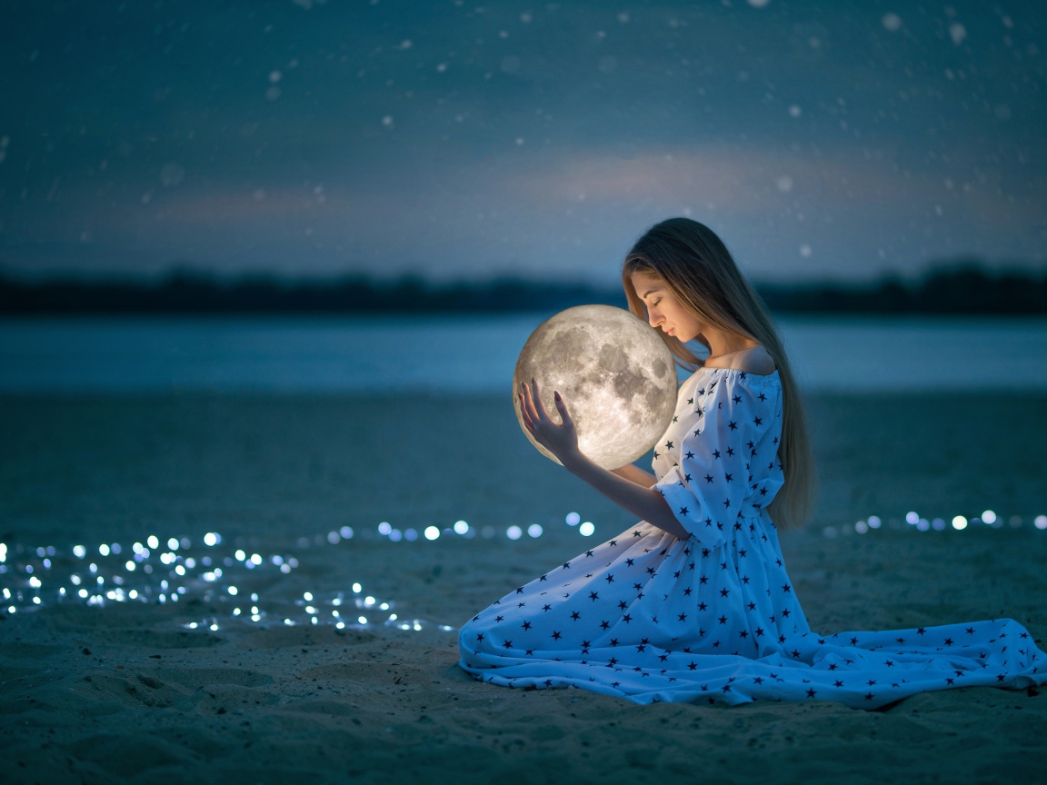 Молодая девушка в красивом платье с луной в руках на песке