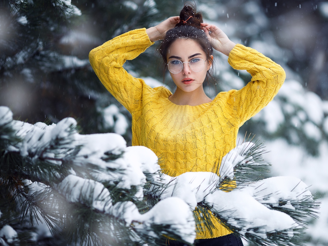 Молодая девушка в очках у заснеженной еловой ветки
