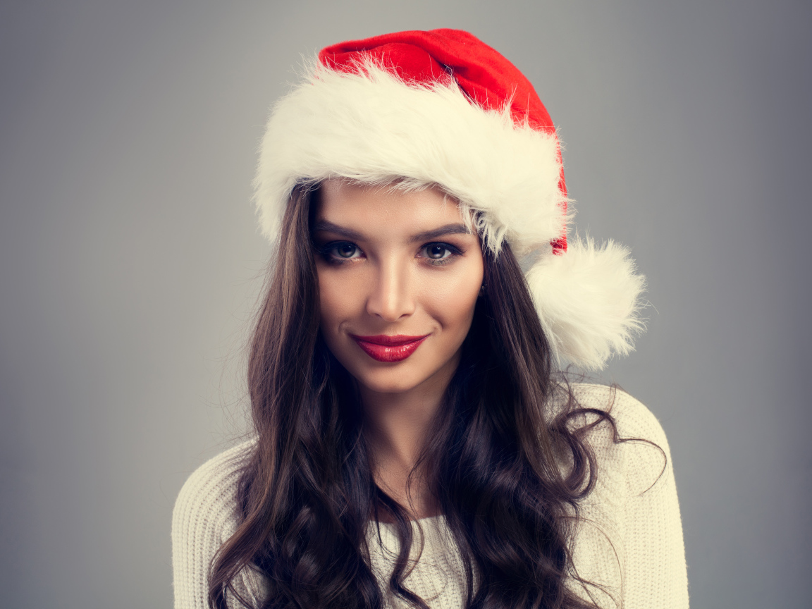 Красивая брюнетка в новогодней шапке на сером фоне