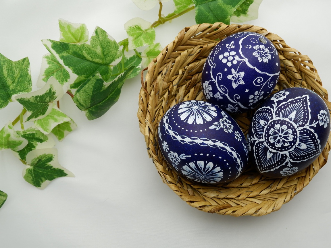 Три раскрашенных яйца в корзинке на столе с веткой 