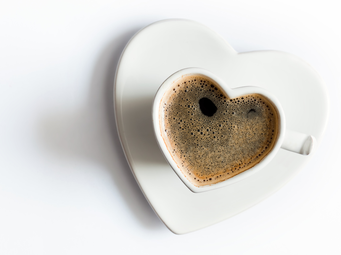 Красивая белая чашка в форме сердца с кофе на белом фоне