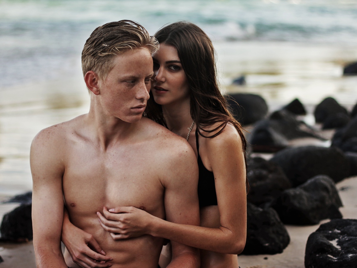 Влюбленная пара сидит на камнях на берегу моря 