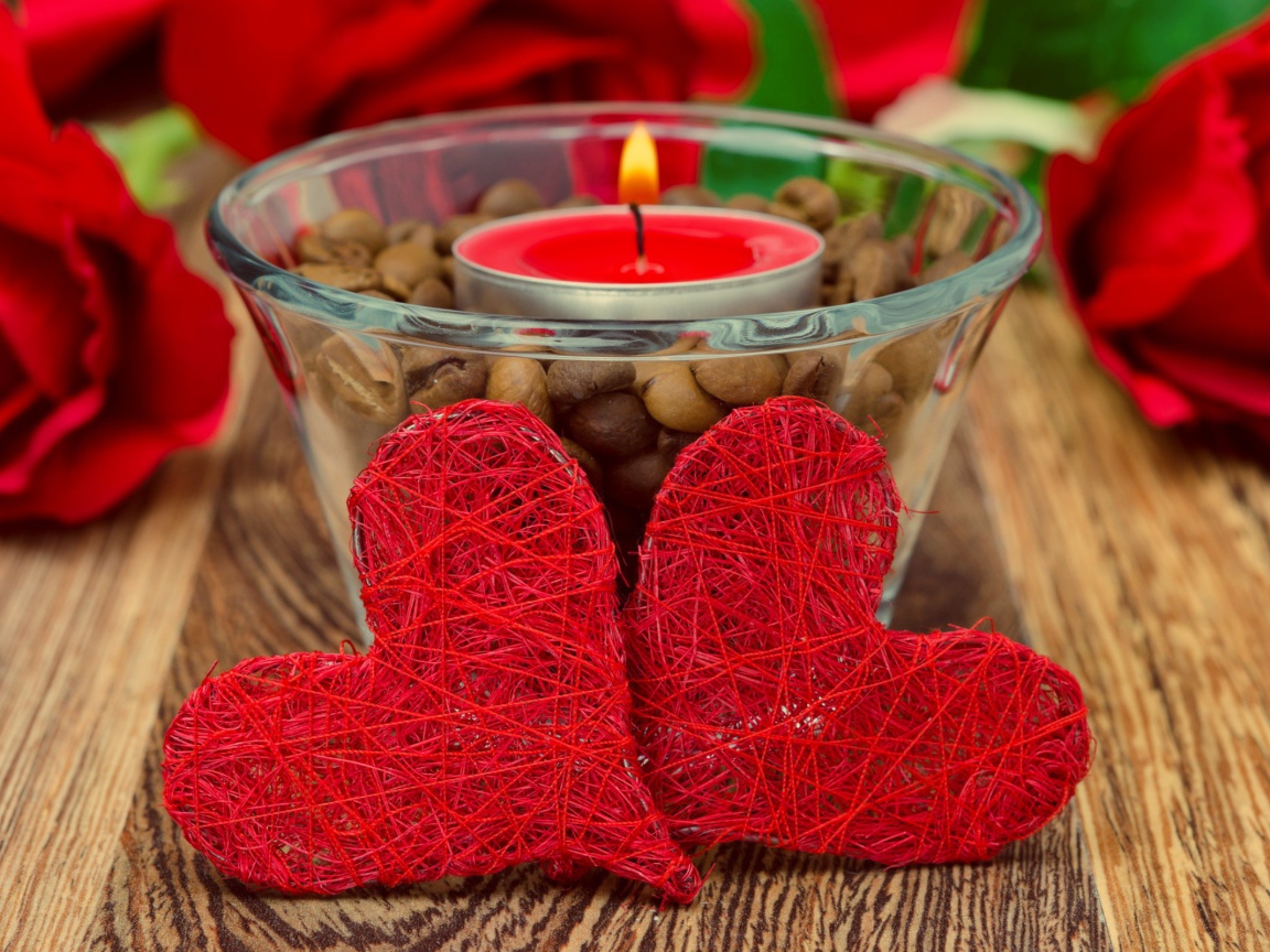 Two red wicker hearts on a table with a burning candle