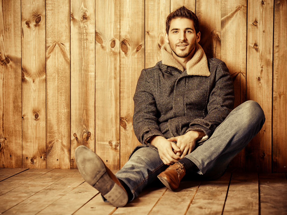 Молодой мужчина в пальто сидит у стены