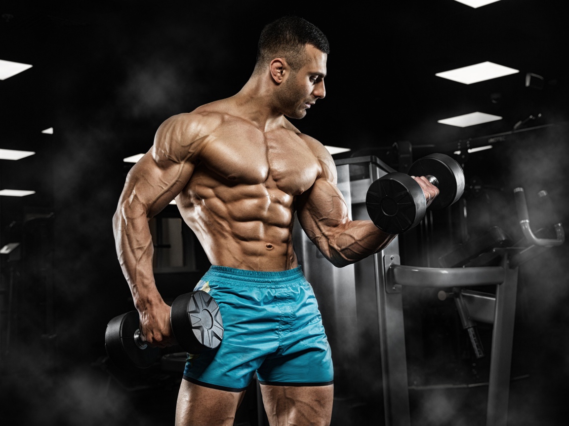 Сильный накаченный мужчина в шортах с гантелями в руках 