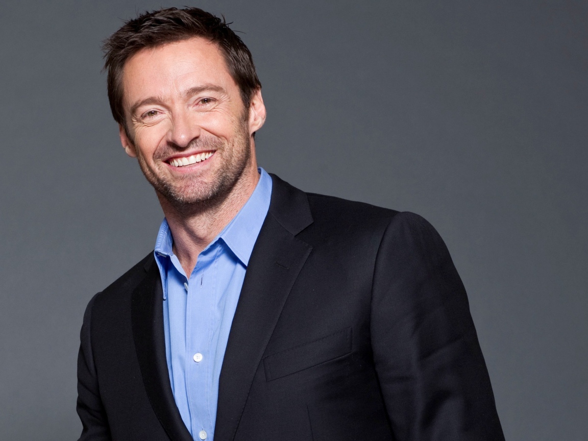 Улыбающийся мужчина, актер Хью Джекман  в костюме на сером фоне