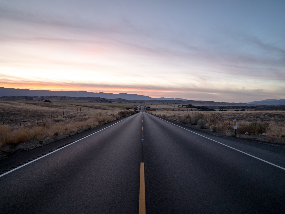 Асфальтная дорога уходит вдаль на фоне неба