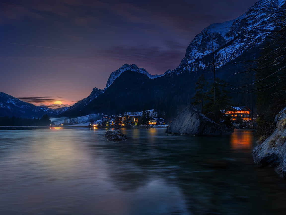 Город у озера на фоне заснеженных гор ночью 