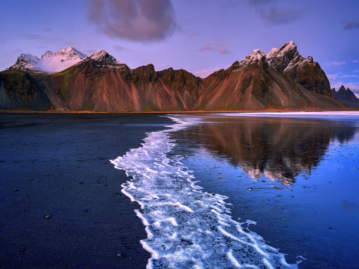 Вода на черном песке на фоне гор 