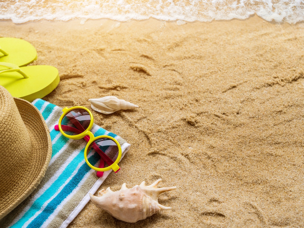 Шляпа, очки, полотенце и ракушки на желтом песке у моря