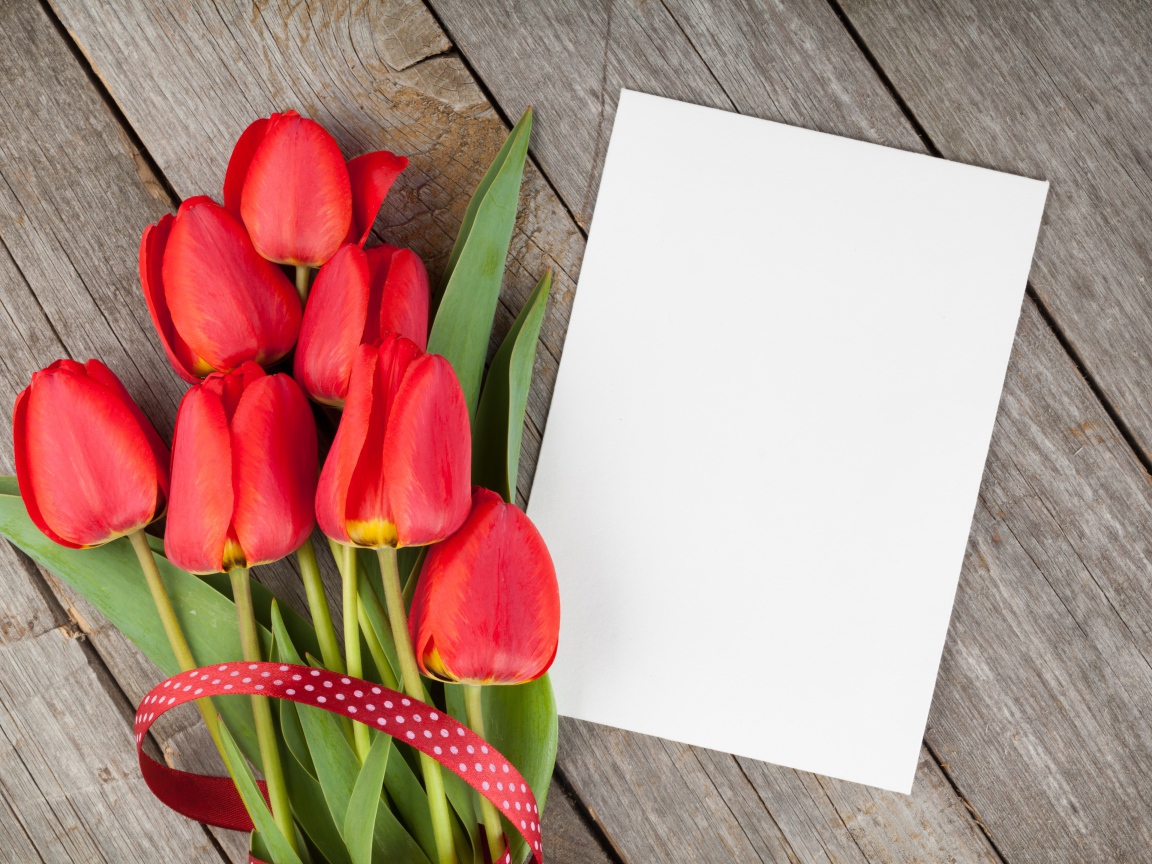 Букет красных тюльпанов с листом бумаги на деревянном столе