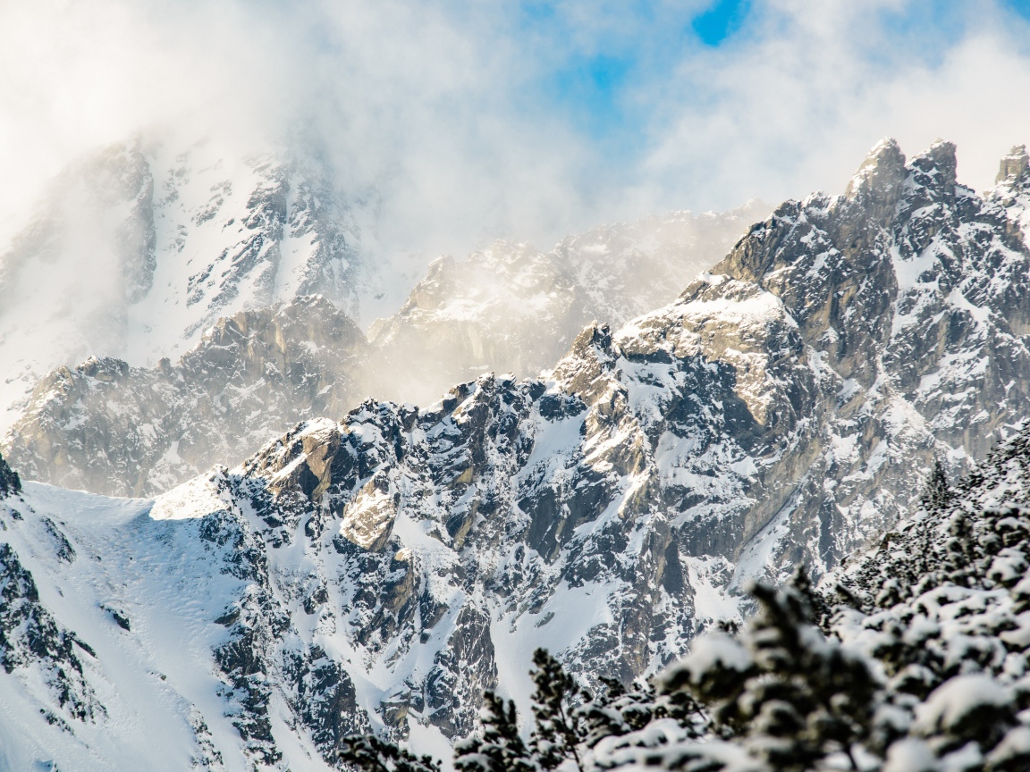 Заснеженные вершины гор под белыми облаками в голубом небе