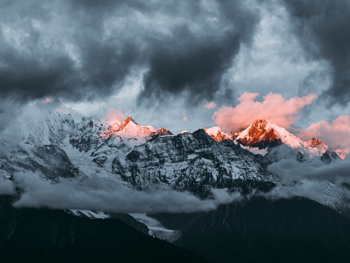 Солнце на рассвете освещает вершины заснеженных гор 