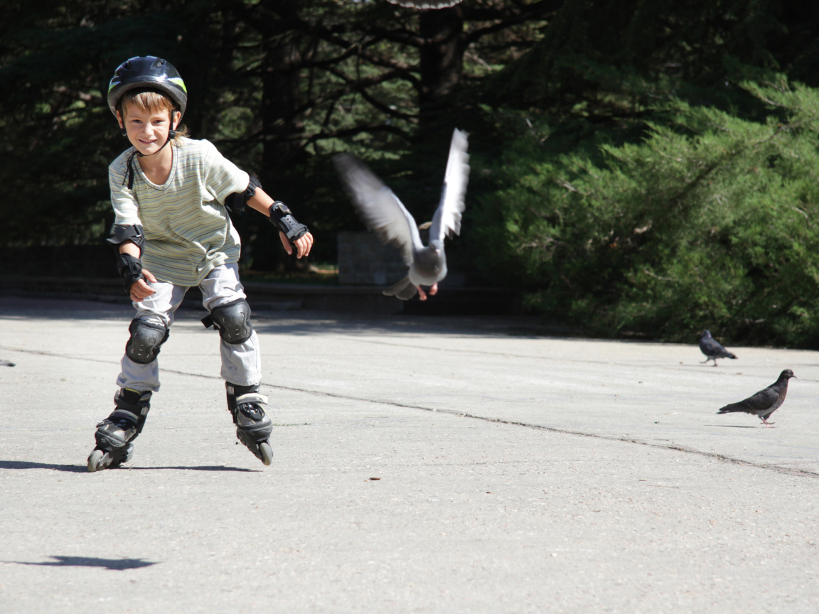 Мальчик катается на роликах на асфальте с голубями