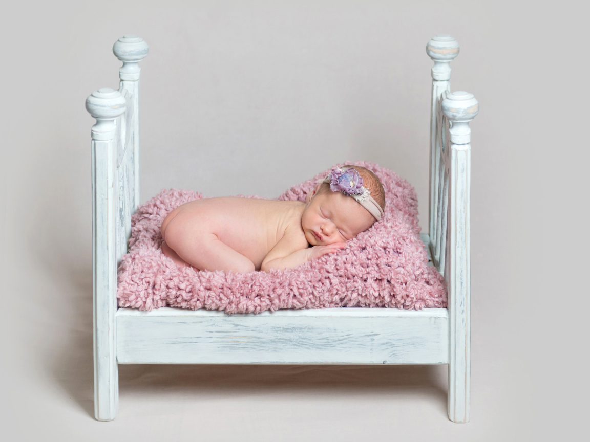 Милый грудной ребенок спит в маленькой кроватке на сером фоне