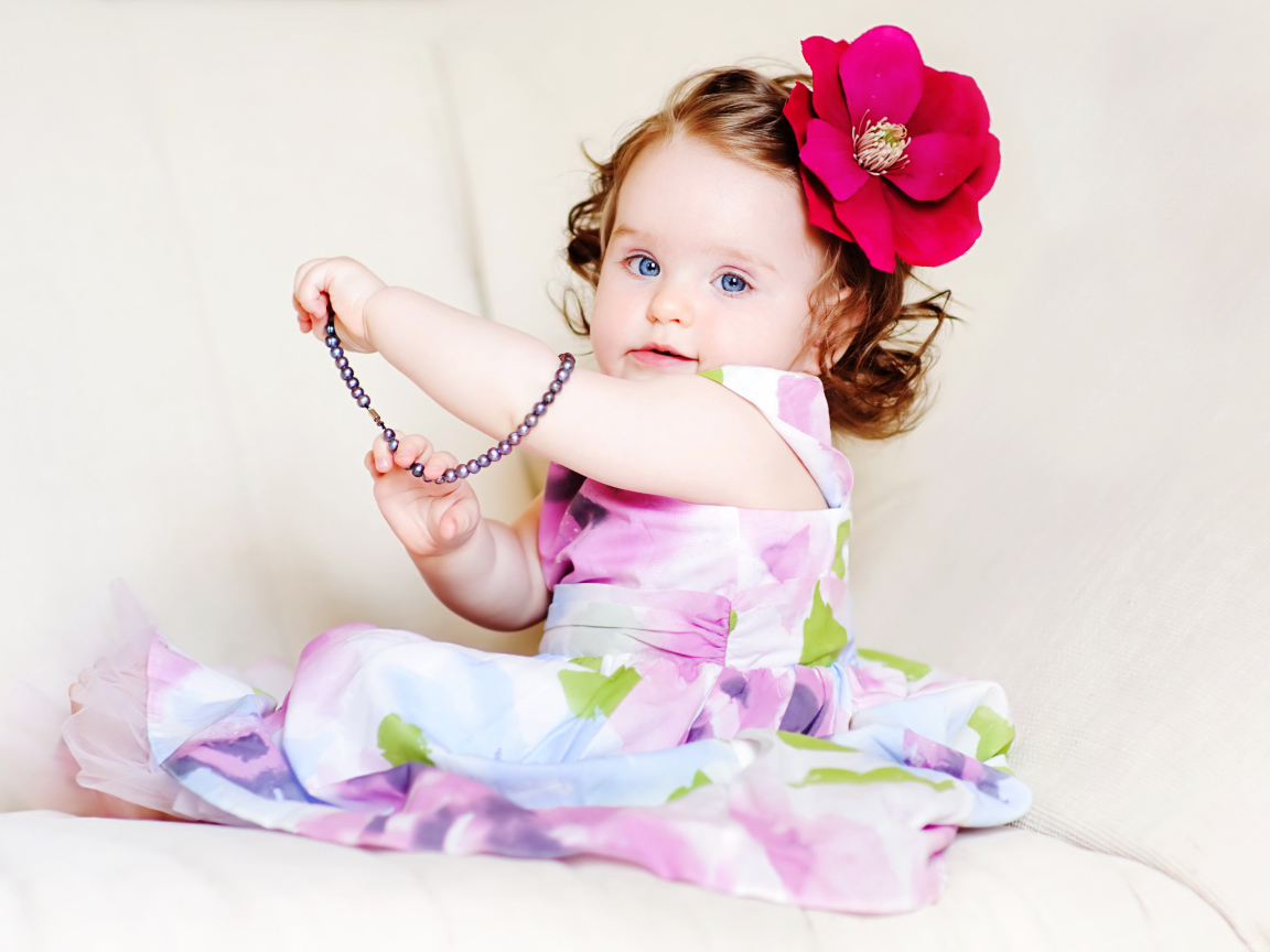 Милая голубоглазая малышка с большим красным цветком в волосах