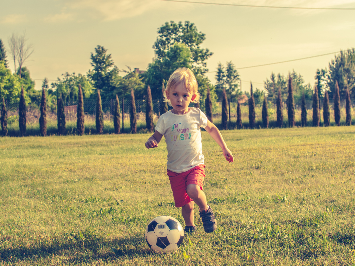Маленький мальчик играет в футбол на зеленой траве