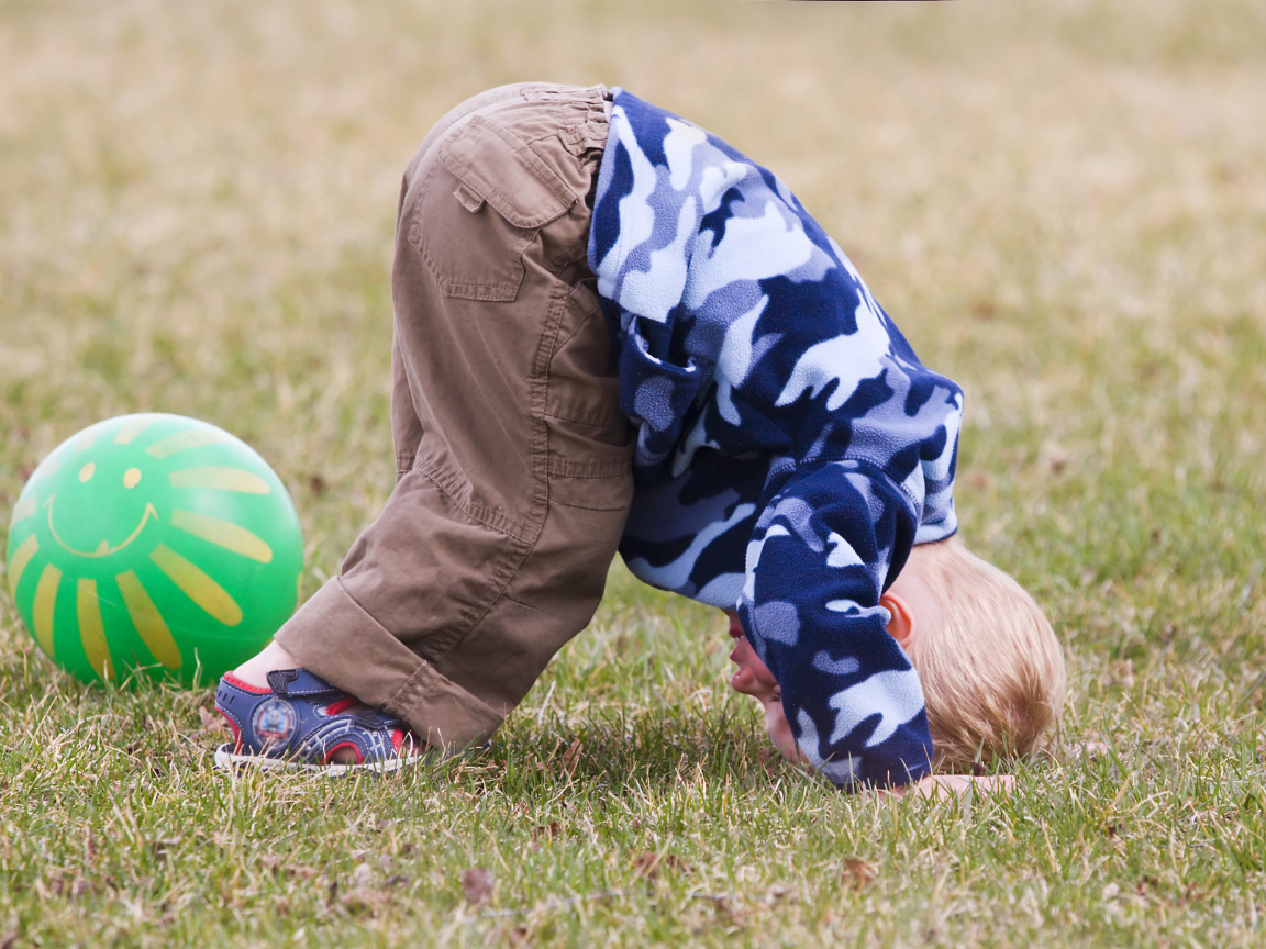 Маленький мальчик играет на траве с мячом