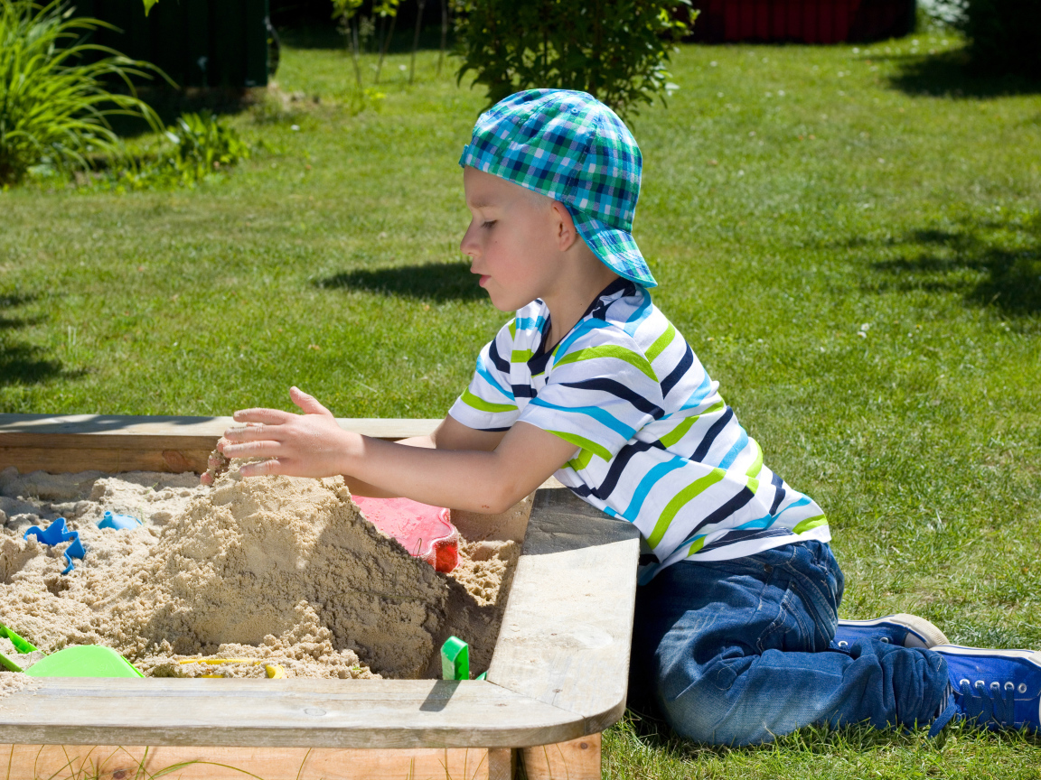 Маленький мальчик играет в песке на зеленой траве
