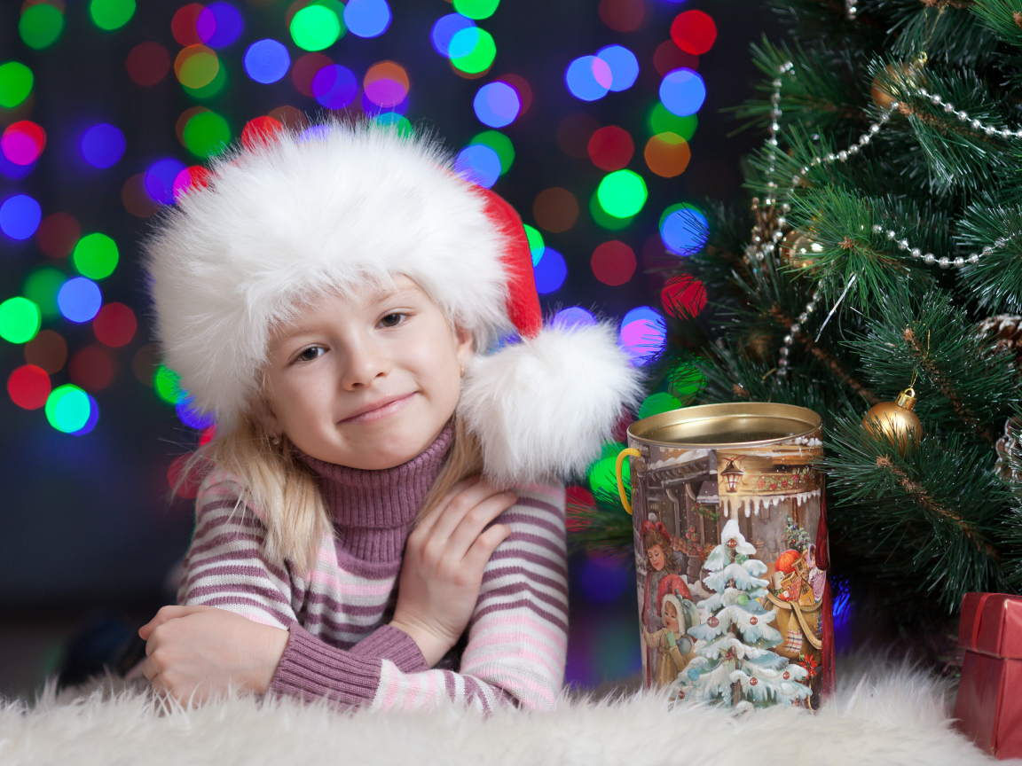 Маленькая девочка в новогодней шапке у елки