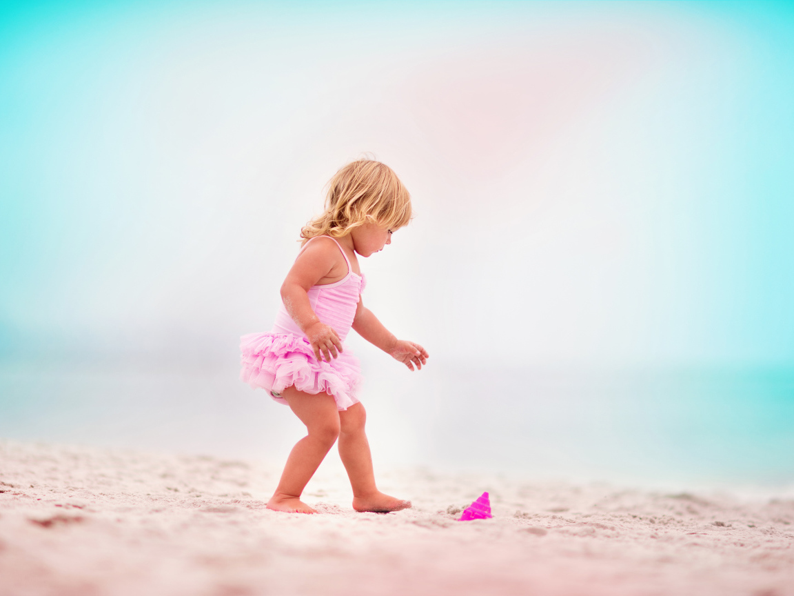 Маленькая девочка в розовом купальнике на песке