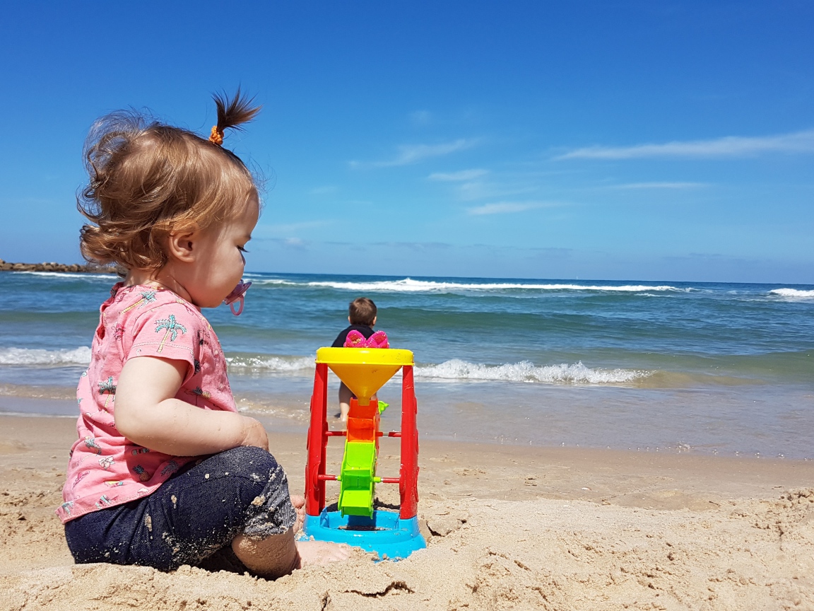 Маленькая девочка играет на песке у моря