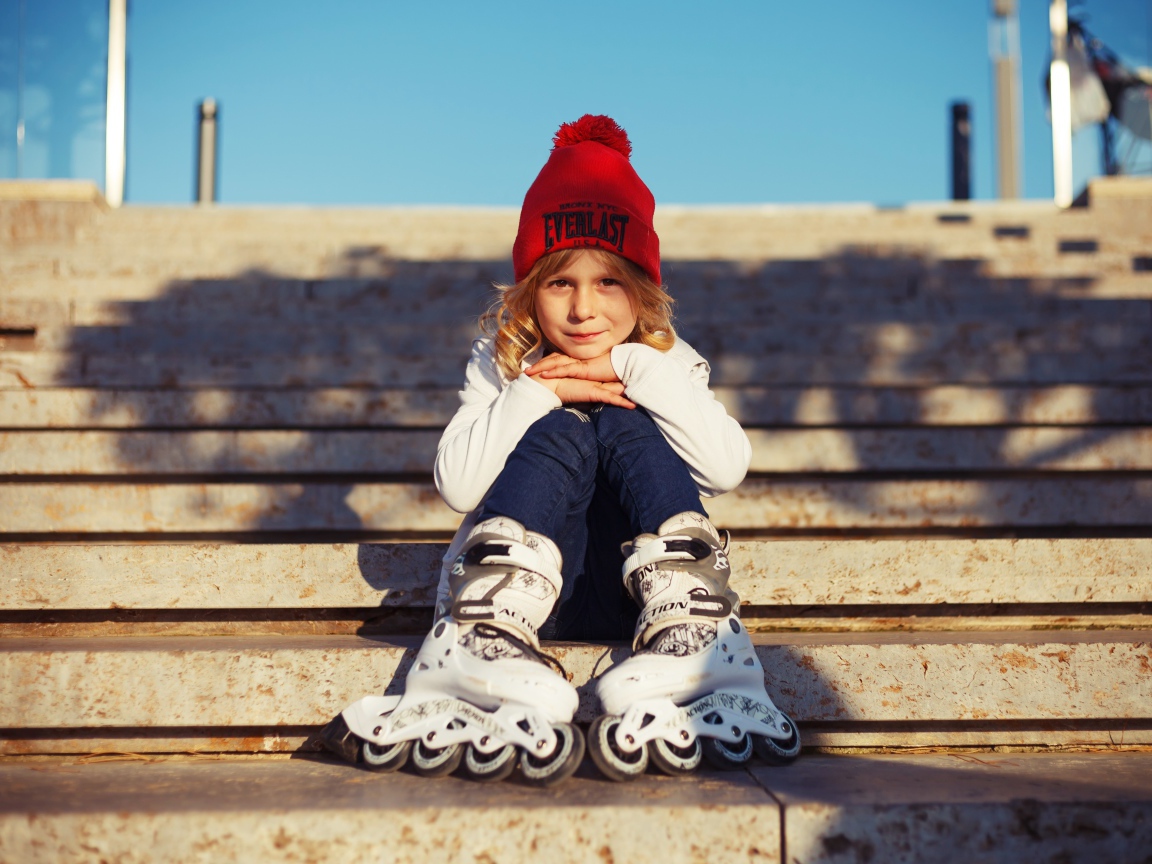 Маленькая девочка в роликах сидит на ступеньках 