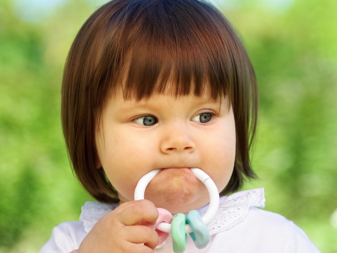 Маленькая девочка с погремушкой во рту