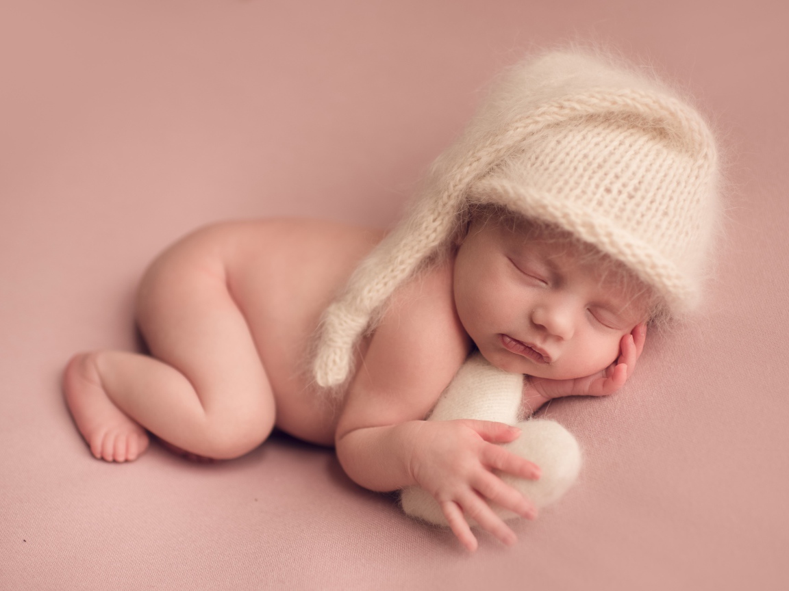 Маленький спящий ребенок в теплой шапке на розовом фоне