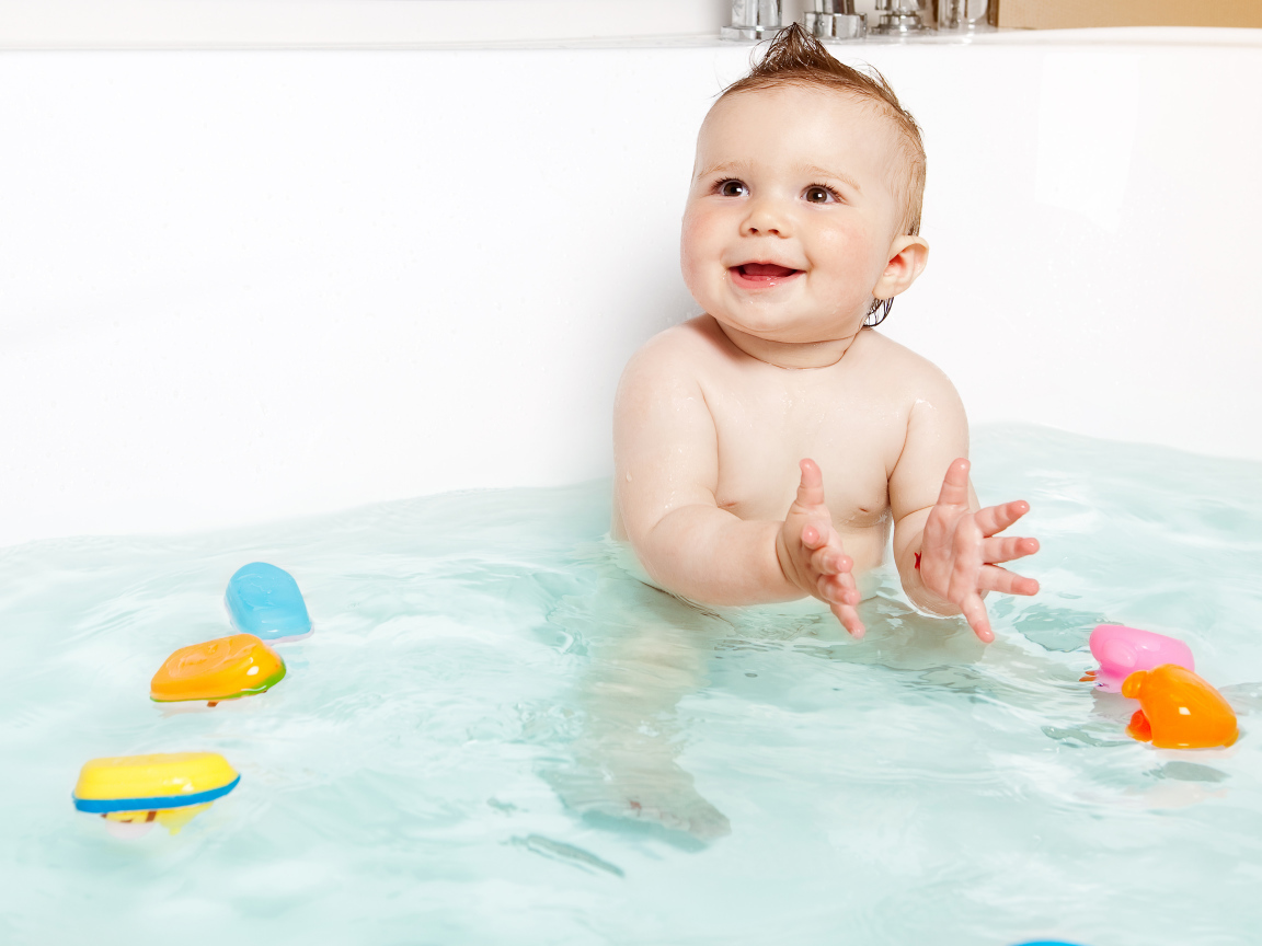 Маленький улыбающийся ребенок с игрушками в ванной 