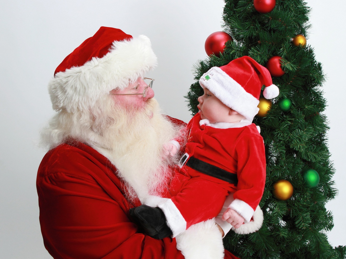 Дед Мороз держит на руках маленького ребенка у елки